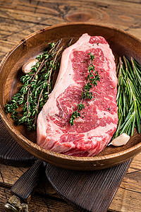新鲜的纽约带状牛肉牛排或带香草的木盘里脊肉。