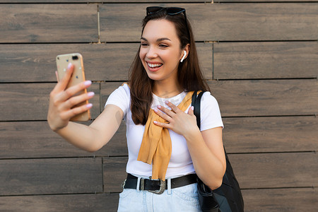 照片中，穿着休闲服的美丽快乐的年轻女子站在街上，通过手机与智能手机交流，玩得开心，心情愉快