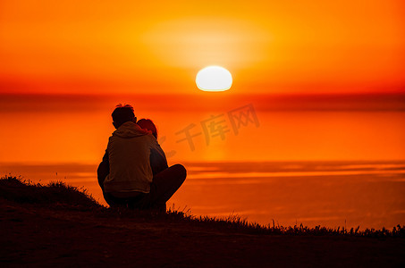 海面上燃烧着红色的夕阳，一对年轻夫妇的剪影