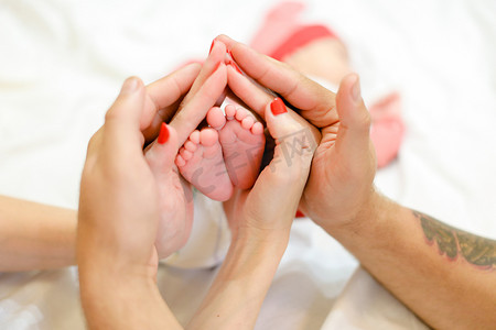 母亲和父亲的手在白色背景下抱着新生儿的婴儿腿。