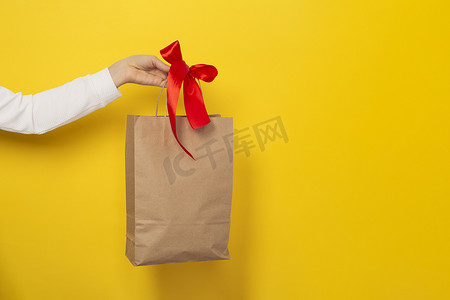 女性手持大礼品袋，由棕色牛皮纸制成，带有红色蝴蝶结。