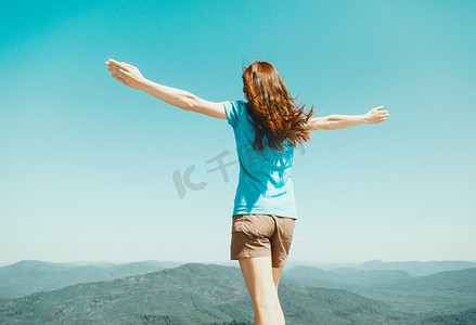 女人站在天空和山脉的背景上举起双臂。