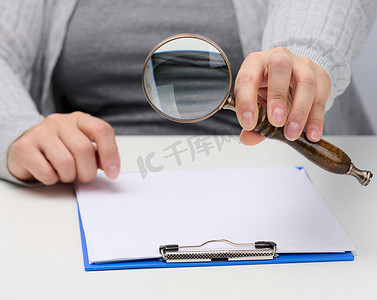 女性手拿着一个木制放大镜在一张放有文件的白色桌子上。