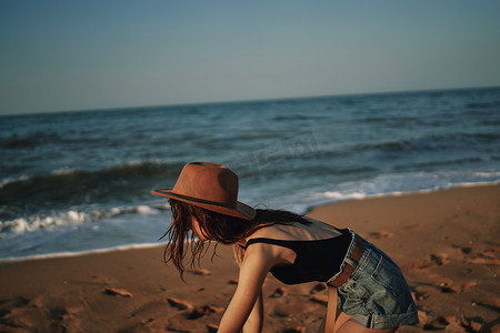 上海夕阳摄影照片_戴着帽子的漂亮女人走在沙滩上海洋旅行