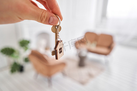形状门摄影照片_男人手拿着钥匙和房子形状的钥匙扣。