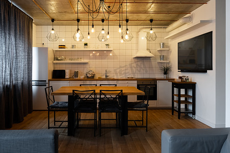现代斯堪的纳维亚风格的厨房室内设计，配有大木桌和椅子，搭配浅色木地板、明亮的白色墙壁和带电视、电器和悬挂灯泡的家具