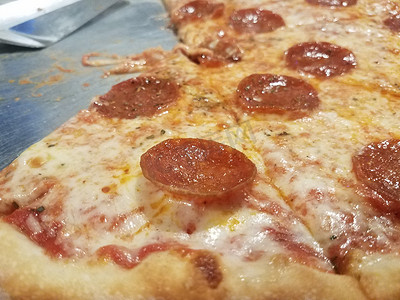 带抹刀的金属托盘上的油腻奶酪和意大利辣香肠披萨