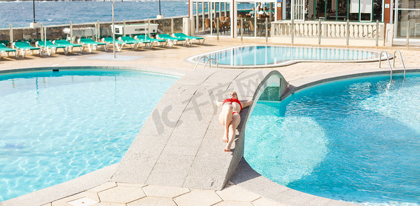 晒水摄影照片_在游泳池附近晒日光浴的年轻女子。