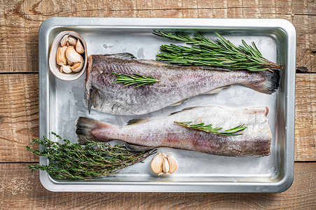 全鱼摄影照片_钢制厨房托盘中的生鳕鱼全鱼，配以百里香和迷迭香。