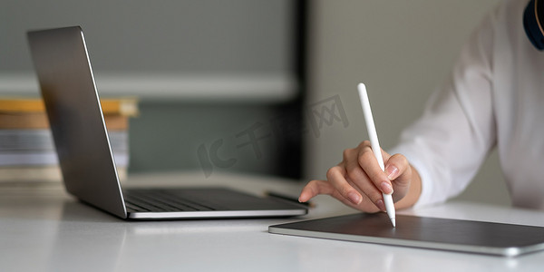 用手写笔在数字记事本上书写，触摸在办公室笔记本电脑上工作的数字平板电脑屏幕上的女人的手。