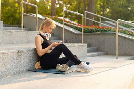 运动和健身年轻成年白人妇女坐在运动垫上的混凝土地板上早上锻炼后在户外夏季公园休息