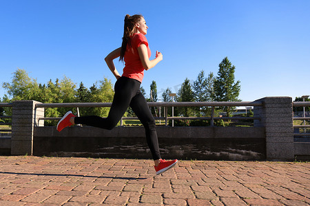 现代年轻女子穿着运动服在户外锻炼时跳跃的照片。