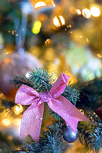 圣诞节粉色摄影照片_圣诞背景，装饰圣诞树绿枝上有美丽的粉色蝴蝶结，散景灯光背景、复制空间、假日、圣诞概念
