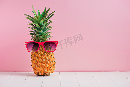 粉红色背景中桌上太阳镜中的滑稽菠萝