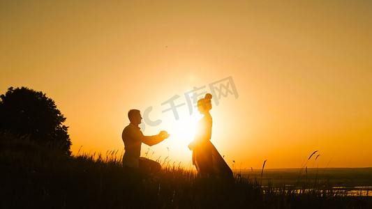 男人跪下向女人求婚的浪漫剪影-情侣在日落时订婚-把戒指女孩的手指