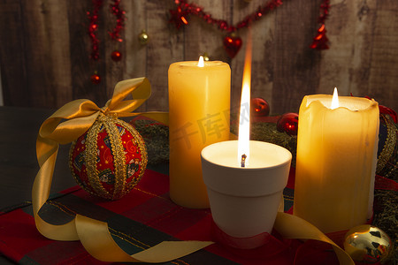 圣诞桌布上点燃的蜡烛，火焰大，松枝周围，剪纸小玩意，点燃的蜡烛，木制背景上挂着圣诞装饰，具有散景效果
