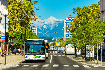 卢布尔雅那 — 2019 年 9 月，斯洛文尼亚：一条街道的景色，背景是公共交通、人行横道、现代建筑和白雪皑皑的阿尔卑斯山