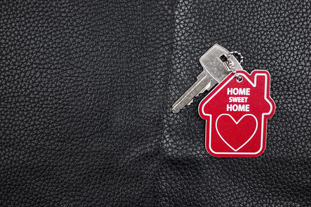甜蜜的家写在红色钥匙圈上，黑色皮革背景上的家形状。