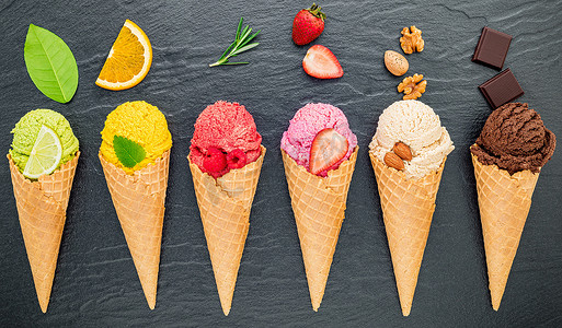 霜果实摄影照片_各种冰淇淋口味的锥体蓝莓、酸橙、开心果、杏仁、橙子、巧克力、香草和咖啡设置在深色石头背景上。