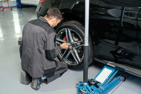 汽车修理厂机械更换车轮使用千斤顶和电钻松开螺栓。服务或更换的概念。