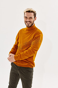 穿着橙色毛衣和裤子的金发快乐男人在浅色背景中笑着
