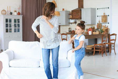 儿童歌曲大赛摄影照片_快乐的母亲带着小女儿在家里的客厅里随着最喜欢的歌曲跳舞。