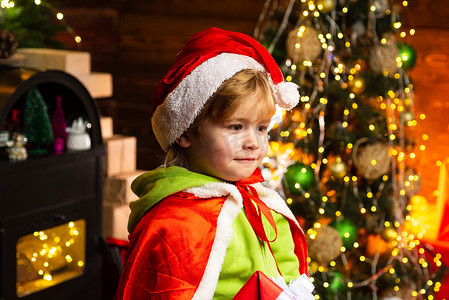 圣诞树背景下戴着圣诞老人帽子的快乐小孩。