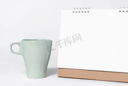 带杯子的空白纸螺旋日历，用于在白色背景上进行样机模板广告和品牌推广。