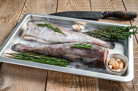 钢制厨房托盘中的生鳕鱼全鱼，配以百里香和迷迭香。