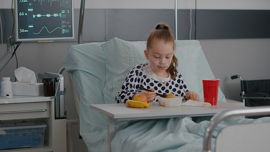 孩子住院摄影照片_住院儿童在康复检查期间卧床休息吃健康食品的画像