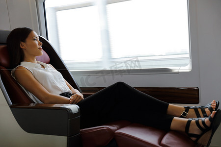 优雅的女士在舒适的头等舱座位上放松，在旅行期间在火车上有更多的腿部空间。