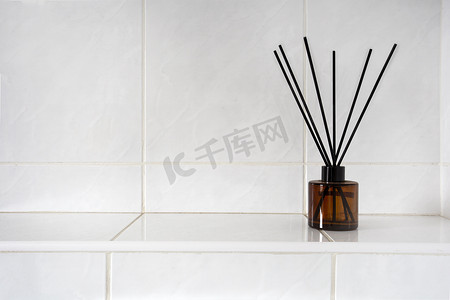 在厕所或浴室的玻璃瓶中香薰棒靠近白色瓷砖墙，有复制空间、香水和竹制奢侈品