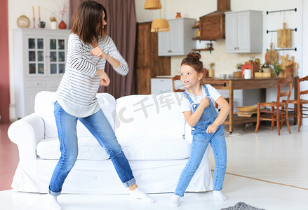 快乐的母亲带着小女儿在家里的客厅里随着最喜欢的歌曲跳舞。