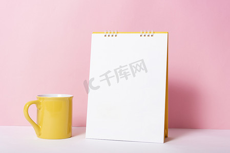 带杯子的空白纸螺旋日历，用于在粉红色背景上进行模型模板广告和品牌推广。