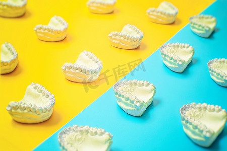 隐形牙套摄影照片_蓝色和黄色背景的正畸牙科主题。适用于正畸牙科治疗的透明隐形牙科对准器或牙套