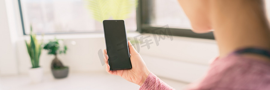 在家使用手机的女性在 5g 数据应用程序上在线观看视频，从后面拿着黑色空屏幕全景横幅生活方式