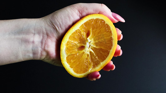 切片水果摄影照片_一只母手挤压了一半新鲜多汁的橙子。
