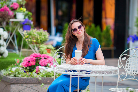 快乐的年轻都市女性，在欧洲的户外咖啡馆里拥有现代手机和咖啡。