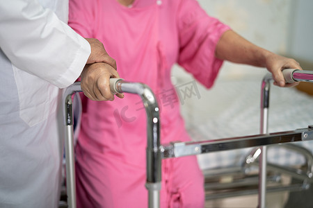 亚洲护士物理治疗师医生护理、帮助和支持老年或老年老妇患者在医院病房与步行器一起行走，健康强大的医疗理念。