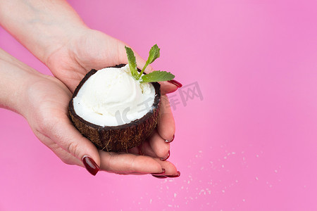 香草冰淇淋球放在新鲜椰子的一半里，手上装饰着粉红色背景的薄荷叶