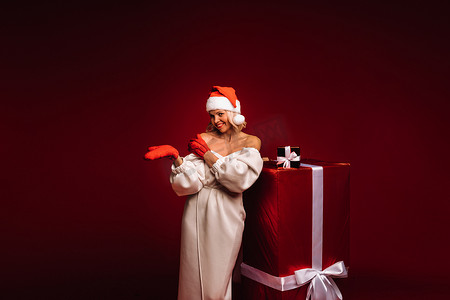 一个微笑的女孩的画像，她穿着白色的裙子，戴着圣诞帽，红色背景上有一件巨大的圣诞礼物