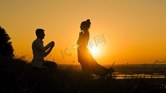 男人跪下向女人求婚的浪漫剪影-情侣在日落时订婚-戴上戒指女孩的手指，滑块拍摄