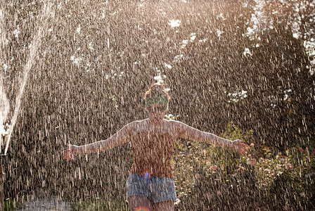 快乐的女孩在阳光下穿过绿色公园的喷泉