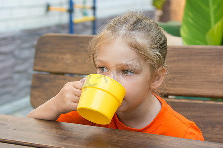 四岁女孩坐在阳台上的桌子旁喝饮料