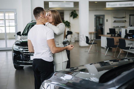 快乐的女人在汽车陈列室买车后拥抱他的丈夫。