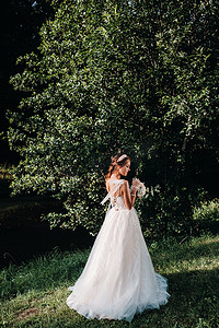 在自然公园里，一位身穿白色连衣裙、手捧花束的优雅新娘的画像。模特穿着婚纱，戴着手套，手捧花束。白俄罗斯
