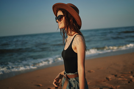 戴着帽子的漂亮女人走在沙滩上海洋旅行