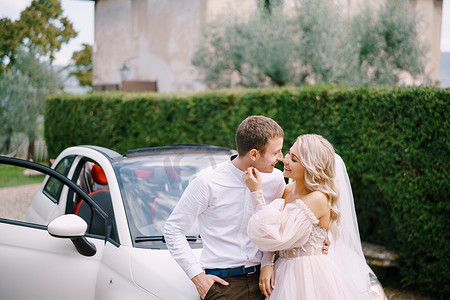 美丽的新娘和新郎靠在一辆敞篷车上，在意大利佛罗伦萨附近托斯卡纳的老别墅里互相看着对方