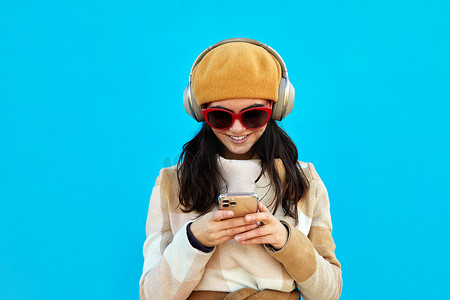戴着耳机浏览智能手机蓝色背景的快乐女性