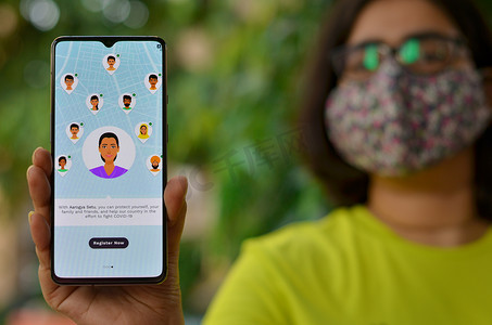 2020 年，印度德里。在家隔离期间，戴口罩的女孩在手机上展示 Aarogya Setu 应用程序。